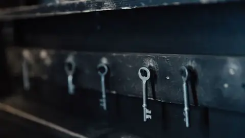 Close-up of antique skeleton keys hanging in a row on a dark wall.