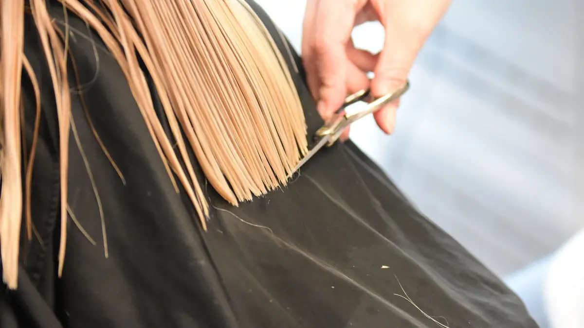 Professional hairdresser cutting blonde hair with scissors in a salon close-up.