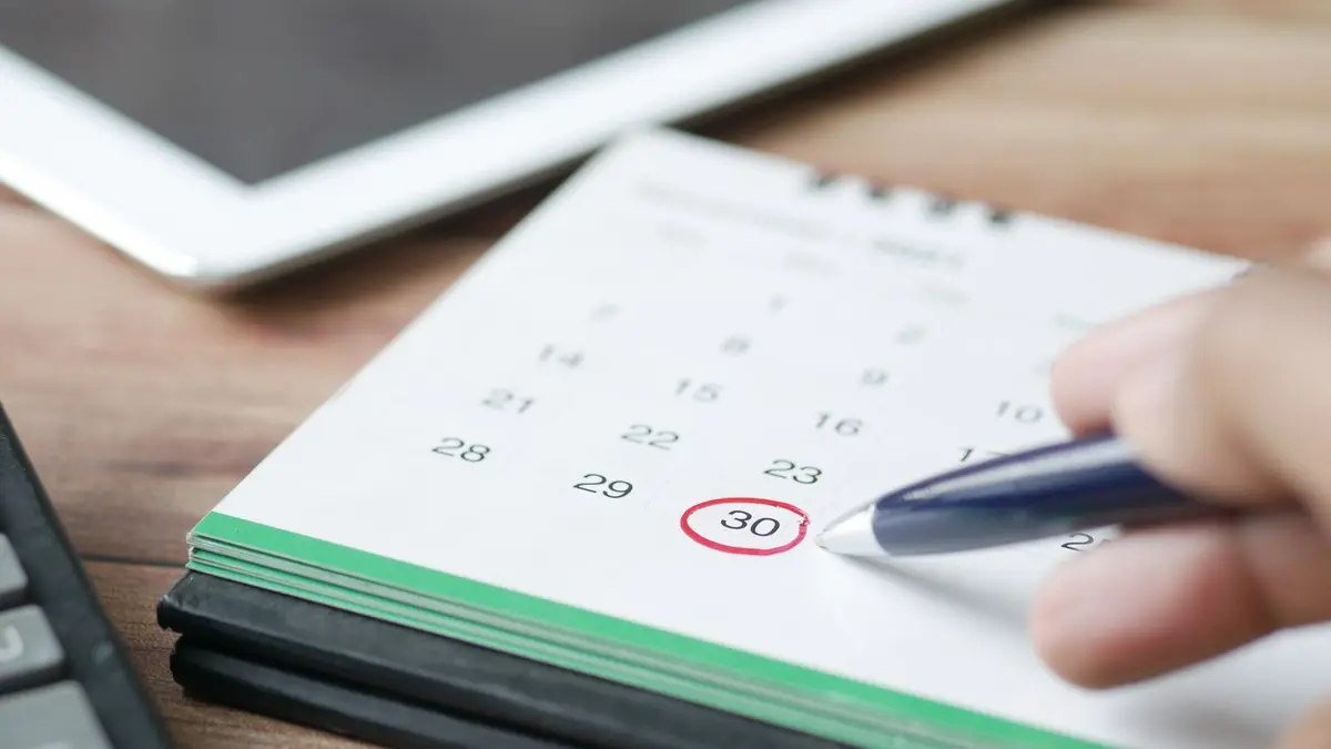 Close-up shot of a hand marking a date on a calendar with a pen, emphasizing planning and scheduling.