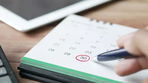 Close-up shot of a hand marking a date on a calendar with a pen, emphasizing planning and scheduling.