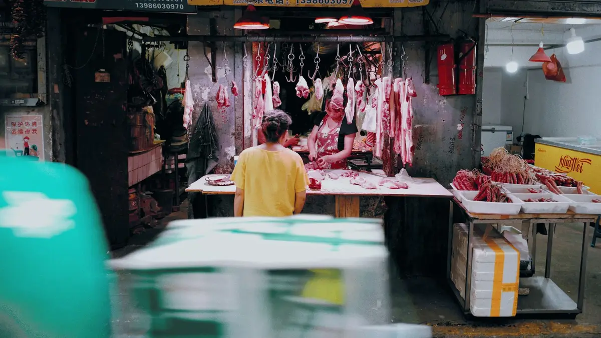 A vibrant scene at a traditional Asian butcher shop with hanging meats and two people interacting.