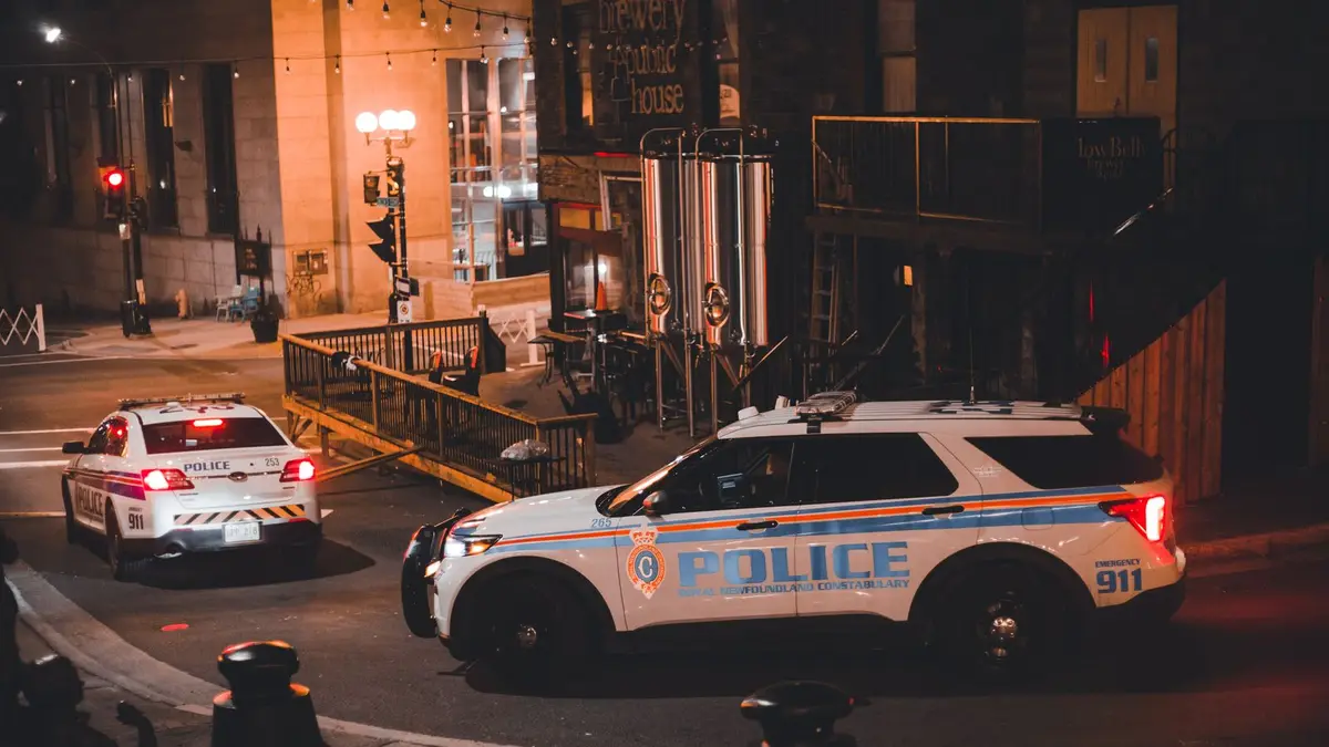 Two police cars patrolling a city street at night with warm lighting creating a dramatic urban mood.