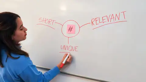 Woman illustrating marketing rules with hashtags on a whiteboard for effective branding strategies.