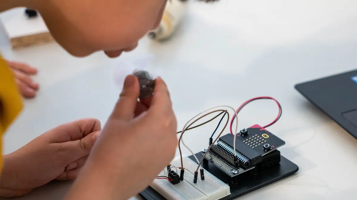 Young child assembling an electronic circuit with a microcontroller on a workbench.