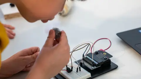 Young child assembling an electronic circuit with a microcontroller on a workbench.