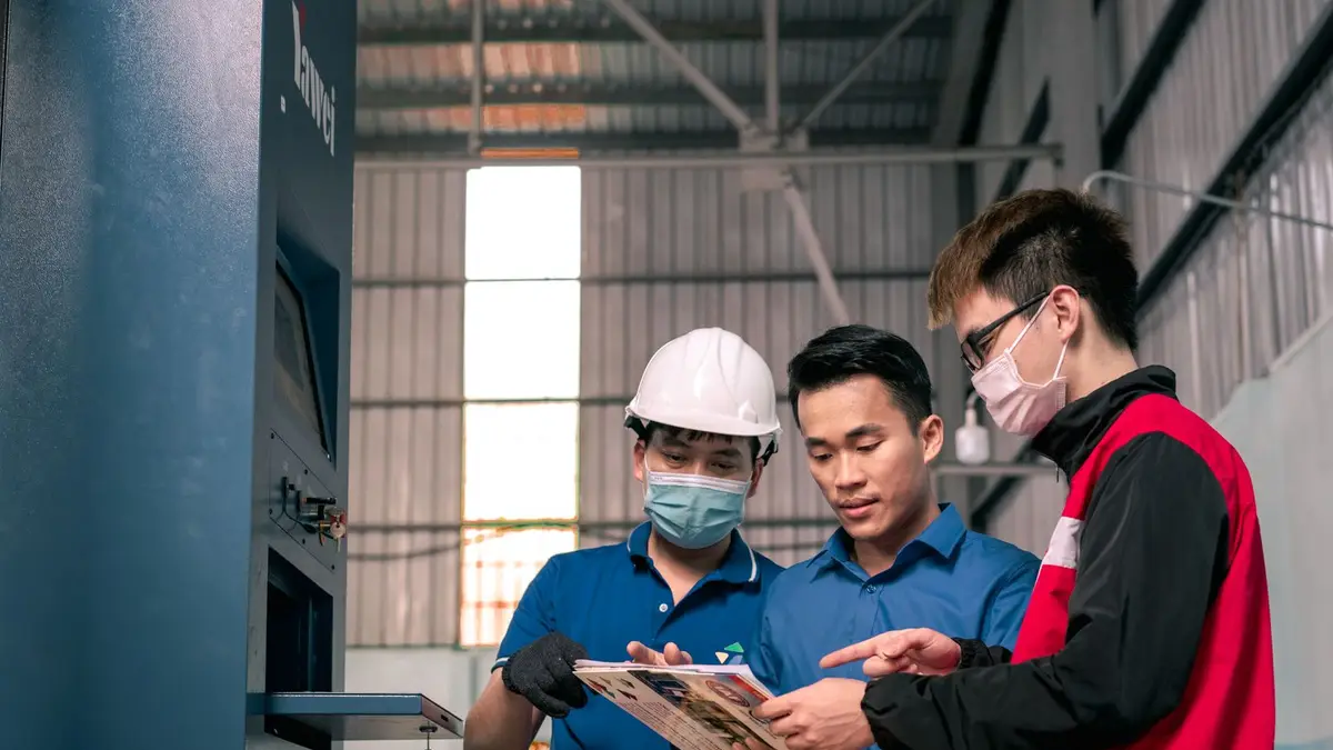 Workers in a warehouse reviewing blueprints, emphasizing teamwork and safety.