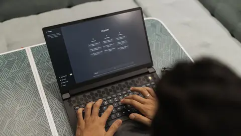 Close-up of hands typing on a laptop displaying ChatGPT interface indoors.