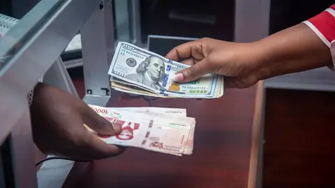 Hands exchanging US and local currency at a bank counter, signifying international finance.