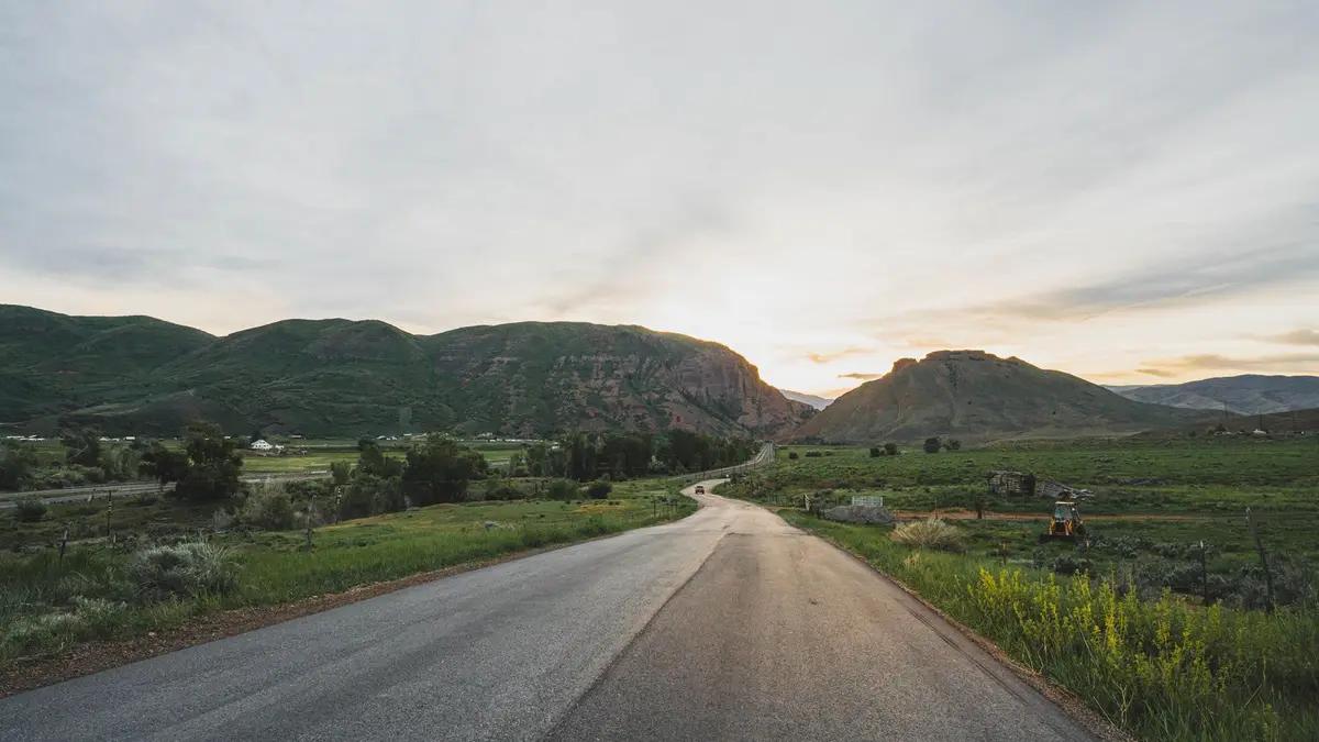 Beautiful rural road winding through a valley with hills at sunset, offering a serene landscape view.