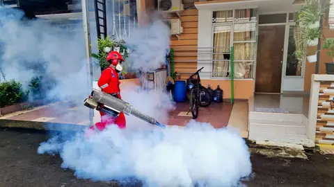 Pest control specialist using a smoke machine to fumigate outside a house.