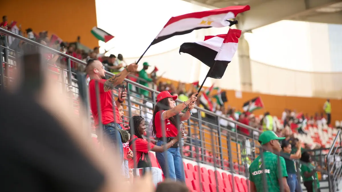 Soccer fans in the stadium wave Egyptian flags, showing their support during a lively sports match.