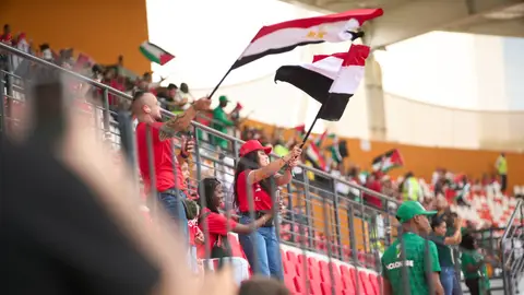 Soccer fans in the stadium wave Egyptian flags, showing their support during a lively sports match.