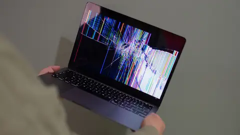 A broken laptop screen displayed with colorful glitch being held by a person.