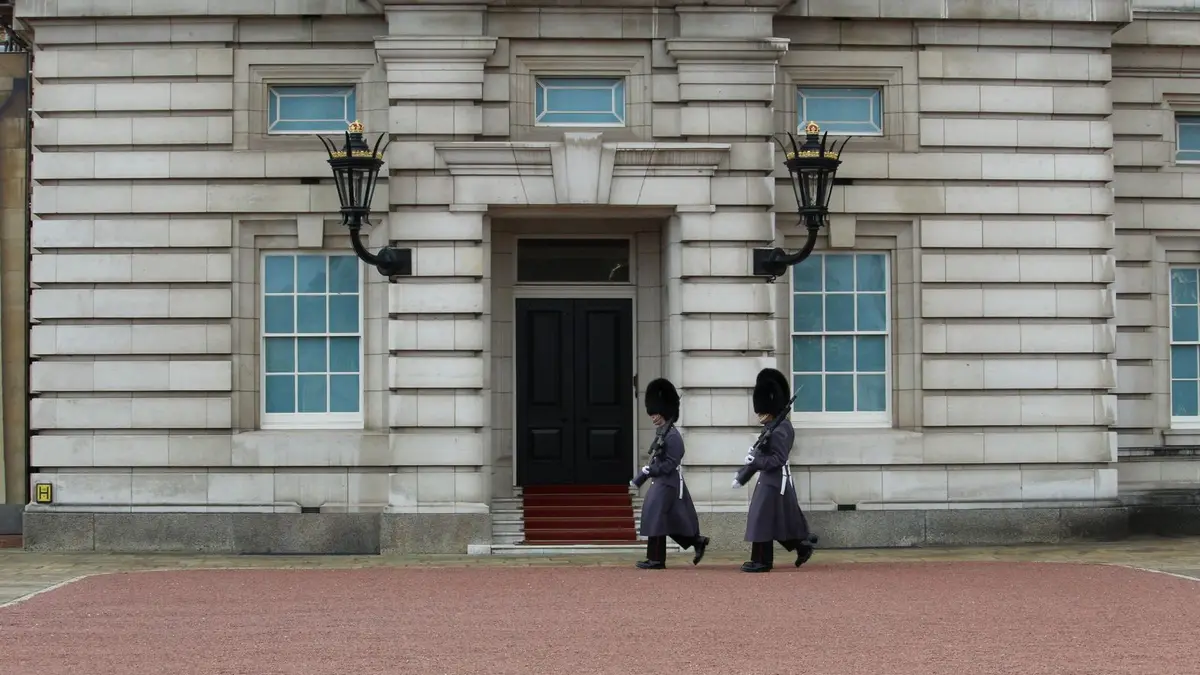 Two royal guards in traditional attire march at Buckingham Palace, London.