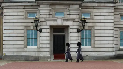 Two royal guards in traditional attire march at Buckingham Palace, London.