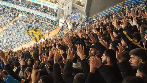Energetic fans with raised hands in a stadium, supporting their soccer team with enthusiasm.