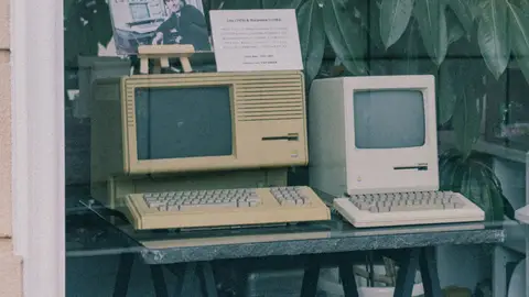 Retro Apple computers with keyboards displayed in a Tokyo store window, showcasing early tech design.