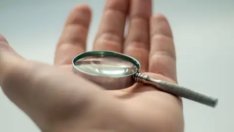 A detailed close-up of a hand holding a magnifying glass, showcasing precision and focus.