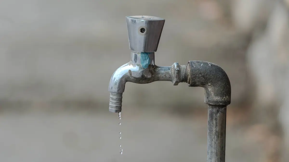 Close-up image of an outdoor water tap with a single droplet falling, highlighting water conservation.