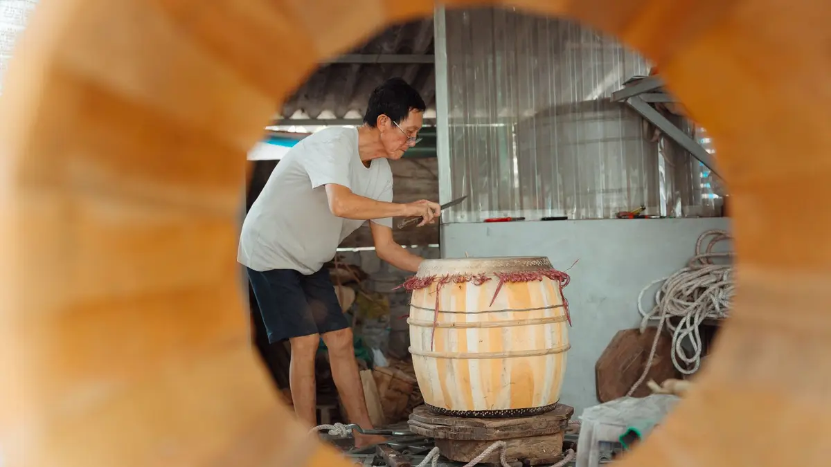 A skilled craftsman shapes a wooden barrel in an artisan workshop through a circular frame.