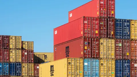 A vibrant collection of stacked shipping containers under a clear, blue sky. Ideal for logistic themes.