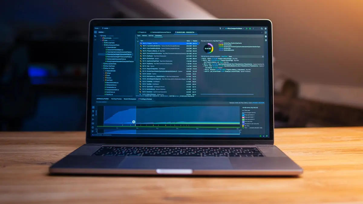 A laptop displaying code on a wooden desk, in a dimly lit workspace.