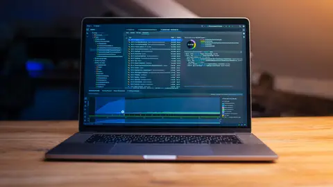 A laptop displaying code on a wooden desk, in a dimly lit workspace.