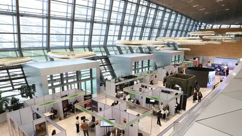 A bustling trade show exhibition inside a modern hall with people networking and exploring booths.