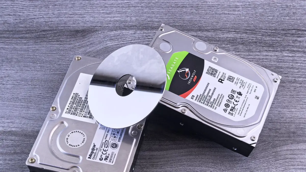Two computer hard drives and a shiny disk displayed on a wooden surface.