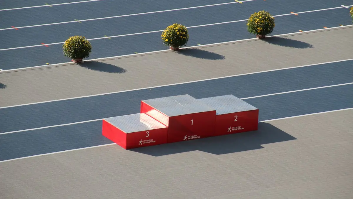 Red podium on a sunny outdoor athletics track with decorative plants.