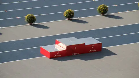 Red podium on a sunny outdoor athletics track with decorative plants.