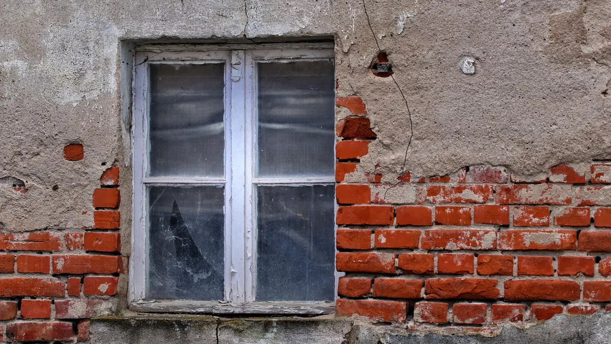 Rustic brick wall with an aged window, showcasing urban decay and architectural texture.