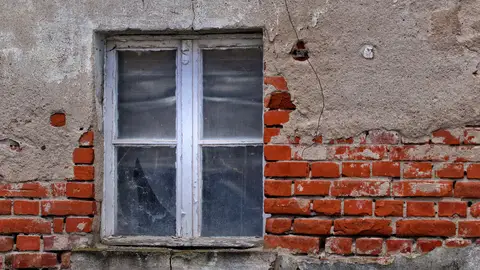 Rustic brick wall with an aged window, showcasing urban decay and architectural texture.