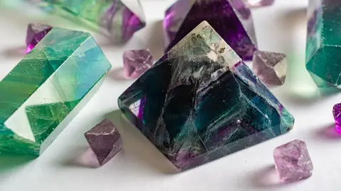 Close-up of colorful fluorite and amethyst crystals in various shapes on a white surface.