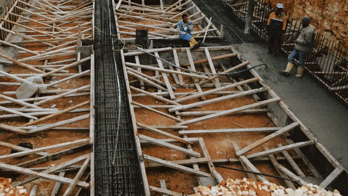 Construction workers at a site with wooden framework in progress, showcasing development.