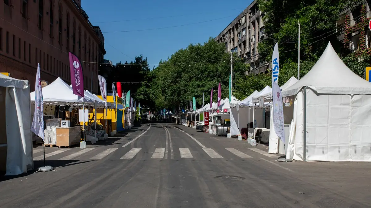 Empty street market setup with white tents and colorful flags on a clear day.