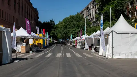 Empty street market setup with white tents and colorful flags on a clear day.
