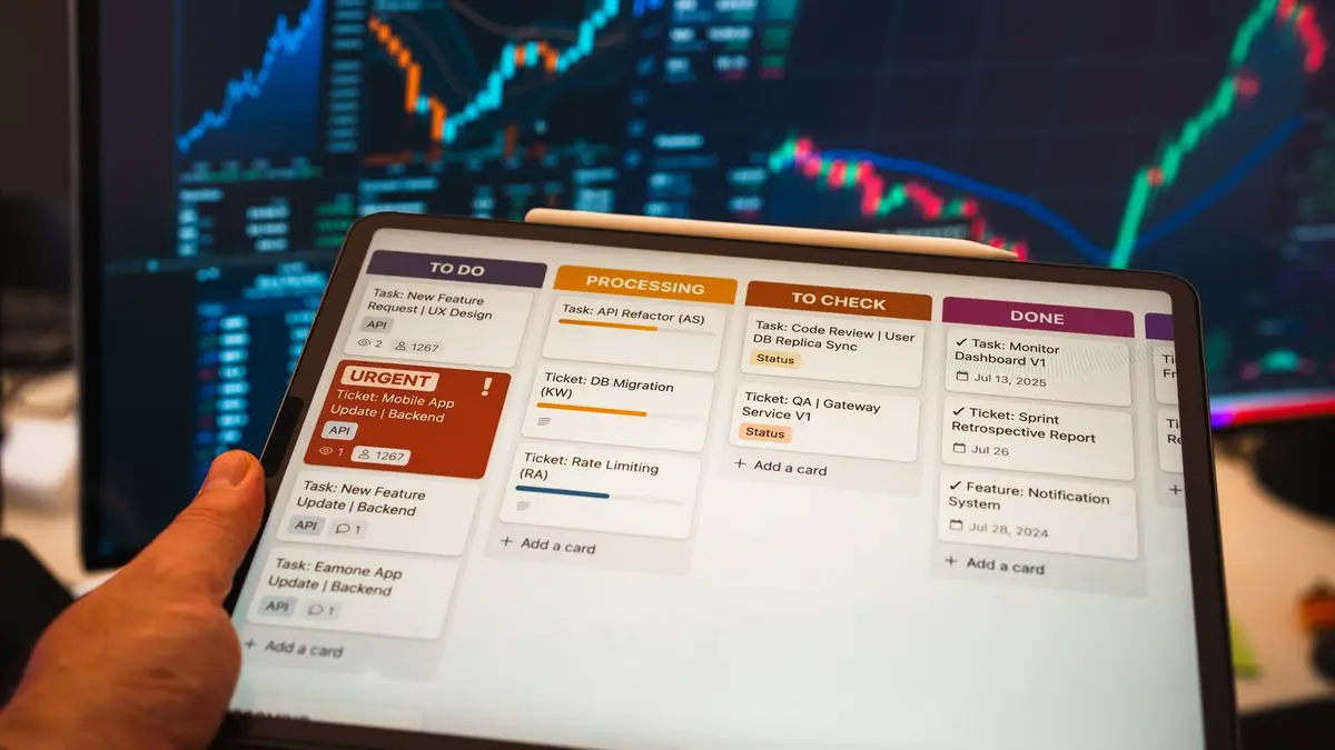 Tablet with business task management app in front of stock chart monitors.