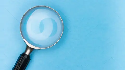Close-up of a magnifying glass on a blue surface, ideal for search and exploration themes.