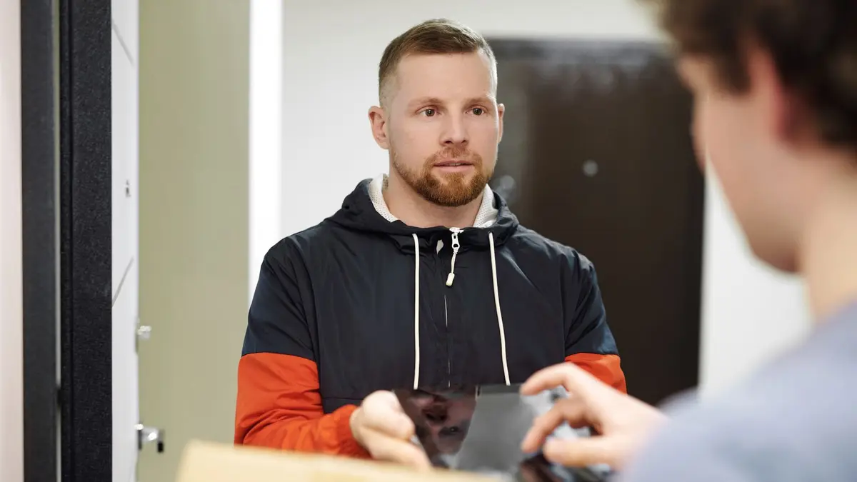 A delivery driver in a hoodie receiving a package indoors, focusing on customer interaction and modern lifestyle.