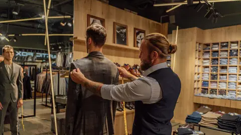 Tailor measuring a client for a suit in a stylish clothing store environment.