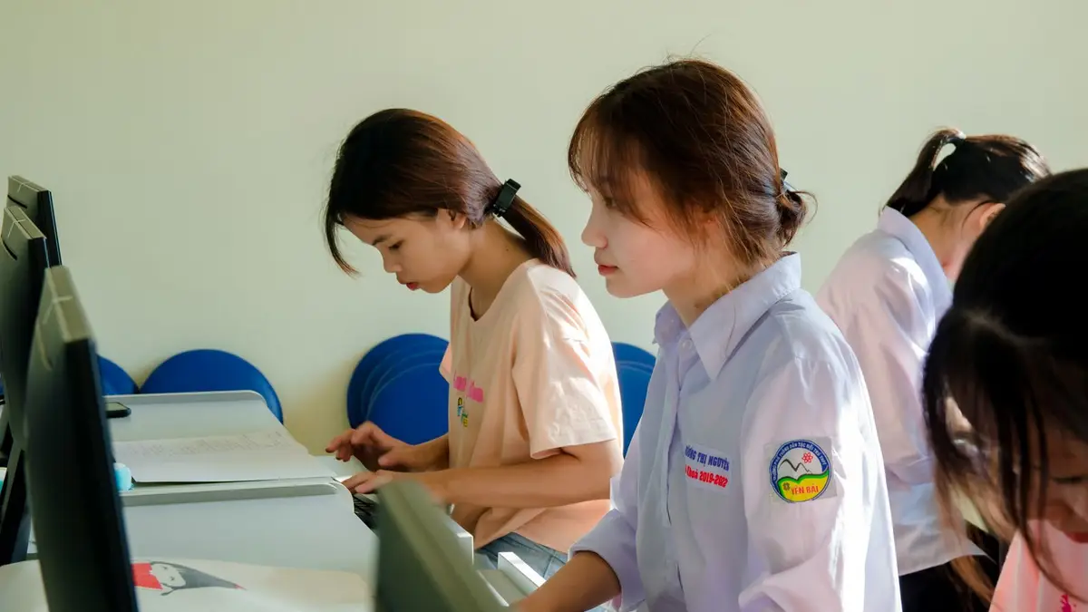 Three young women concentrating on a computer task in a classroom setting.