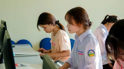 Three young women concentrating on a computer task in a classroom setting.
