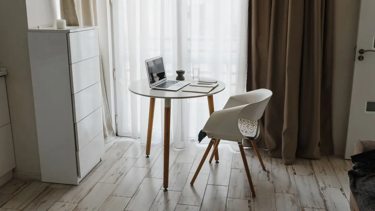 Minimalist home office setup with a laptop, table, and chair by a window for a serene workspace.