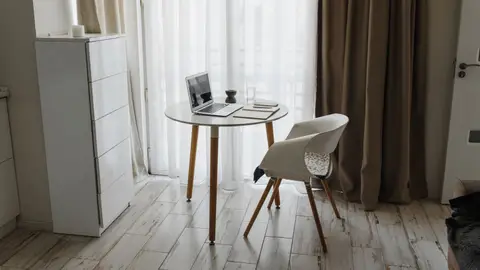 Minimalist home office setup with a laptop, table, and chair by a window for a serene workspace.