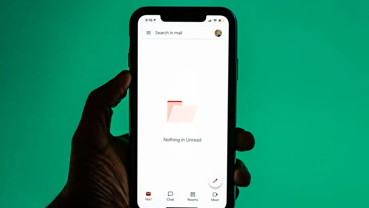 Close-up of a hand holding a smartphone displaying email app against a green background.