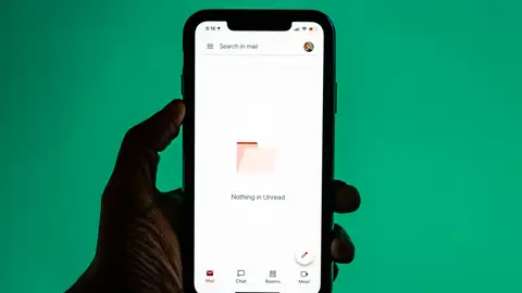 Close-up of a hand holding a smartphone displaying email app against a green background.