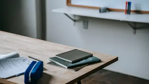 School bench with many copybooks and pencil case placed in light classroom against whiteboard