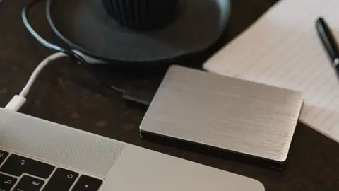 Closeup of an external hard drive connected to a laptop with a USB cable on a desk.