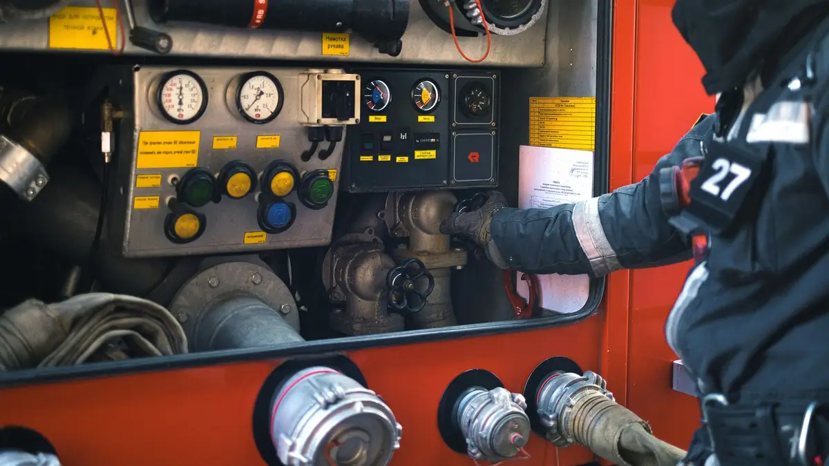 A firefighter in gear adjusting controls on a fire engine during an emergency response.